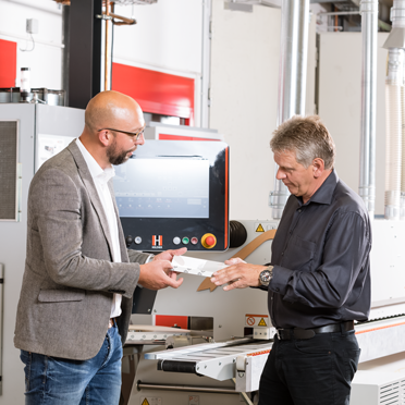 Zwei Männer stehen an einer Kantenanleimmaschine